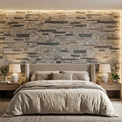 Dormitorio con cabecero tapizado beige y pared de fondo revestida con aplacado imitación piedra gris en formato rectangular apilado, iluminación empotrada cálida, mesitas de madera a ambos lados y ropa de cama en tonos neutros.