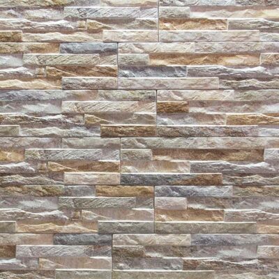 Superficie de revestimiento de pared con textura de piedra irregular en tonos beige, marrón y gris, acabado mate con relieve natural y variación cromática característica de la imitación piedra.