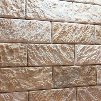 Aplacado de hormigón con efecto piedra en tonos beige y crema, formato rectangular medio, superficie con textura rugosa y veteado natural que imita cantera irregular.