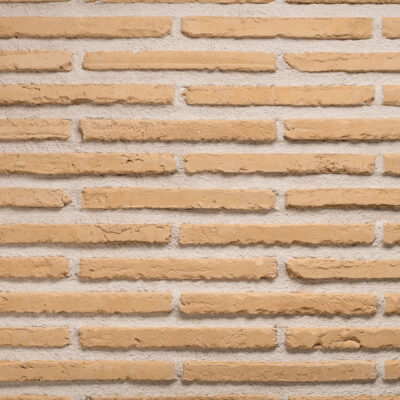 Piezas rectangulares de aplacado hormigón con textura imitación ladrillo en tonos cálidos amanecer, dispuestas en patrón de hiladas corridas. Superficie rugosa y envejecida con variación cromática entre piezas, acabado mate que simula la estética rústica del ladrillo cerámico visto.