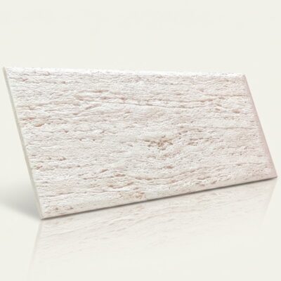 Plaqueta cerámica rectangular con acabado mate y textura rústica imitando piedra natural en tonos marfil claro con vetas irregulares.