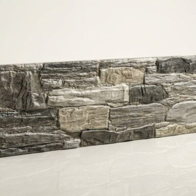 Plaqueta rectangular con textura de piedra natural en tonos grises y beige, acabado mate y rugoso. Formato modular apilable para revestimiento de pared.
