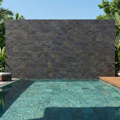 Área de piscina con revestimiento de pared en plaquetas imitación piedra grafito, rodeada de vegetación tropical y zonas de descanso con madera y textiles.
