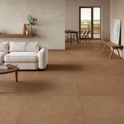Espacio de salón y comedor con suelos en gres porcelánico efecto piedra en tonos terracota e ivory. El pavimento de gran formato se extiende por toda la zona, combinado con mobiliario de madera natural y paredes en tonos neutros.