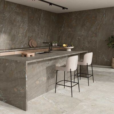 Cocina de diseño contemporáneo con suelo porcelánico imitación piedra en tonos grises y paredes revestidas del mismo material. Isla central con frente de hormigón, encimera gris marmóreo, taburetes tapizados en crema y detalles en madera natural.
