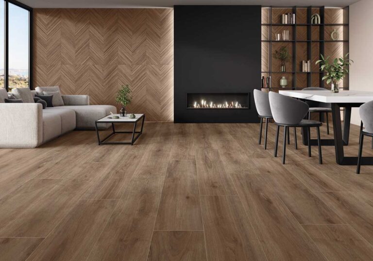Salón contemporáneo con suelos porcelanicos efecto madera nogal en formato tabla, pared de revestimiento en espiga, chimenea lineal negra, mobiliario en tonos grises y estantería de madera con accesorios decorativos.