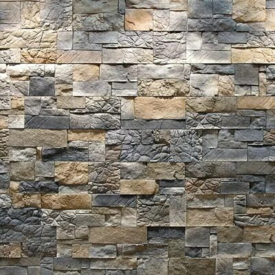 Superficie de revestimiento con imitación de piedra natural en tonos grises, beige y antracita. Textura profunda y relieve marcado que simula piedra irregular apilada, con acabado mate y variación de color entre piezas.