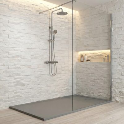 Baño con plato de ducha gris y revestimiento de pared imitación piedra en tonos marfil y beige. Mampara de cristal, grifería de ducha empotrada y nicho con iluminación integrada.