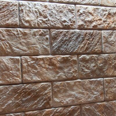 Baldosa rectangular de revestimiento con textura de piedra natural en tonos marrón y beige, acabado rústico mate con relieve irregular.