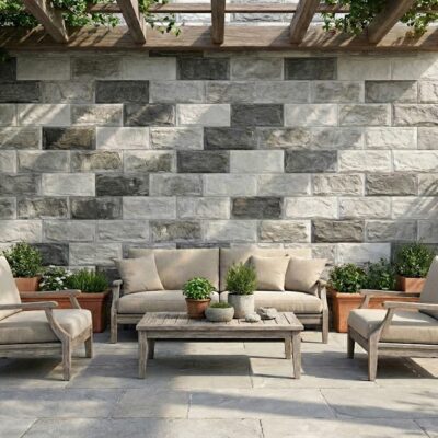 Terraza exterior con aplacado de hormigón imitación piedra Andros Mix Gris en tonos grises y blancos. Zona de descanso con sofá y sillones de madera clara, macetas de barro, y pérgola de madera. Pavimento de losa gris claro.