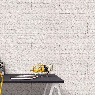 Despacho con pared de revestimiento imitación piedra blanca con textura lisa y acabado mate. Escritorio negro con silla amarilla, pequeño avión decorativo amarillo y accesorios de oficina sobre la superficie.