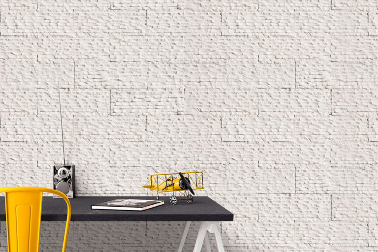 Despacho con pared de revestimiento imitación piedra blanca con textura lisa y acabado mate. Escritorio negro con silla amarilla, pequeño avión decorativo amarillo y accesorios de oficina sobre la superficie.