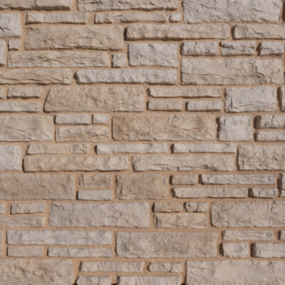 Superficie de revestimiento con textura de piedra natural irregular en tonos beige y gris claro, acabado mate rústico con relieve tridimensional y juntas de mortero visibles.