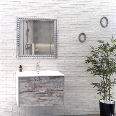 Baño con pared de ladrillo blanco, mueble lavabo suspendido con frente texturizado gris, espejo con marco plateado, y accesorios decorativos. Planta en maceta negra a la derecha.