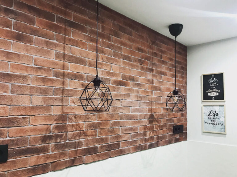 Pared revestida con aplacado efecto ladrillo rojo oscuro y blanco, complementada con dos lámparas colgantes de metal negro de diseño geométrico. Detalles decorativos inspiradores sobre la pared blanca adyacente.