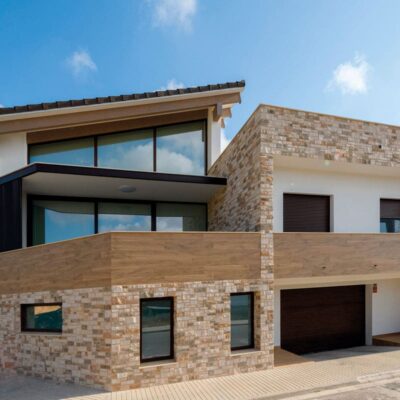 Fachada de vivienda moderna con revestimiento de hormigón imitación piedra en tonos cálidos y rojizos. El aplacado de corteza cubre la base de la construcción, combinando texturas irregulares que evocan piedra natural en exterior.