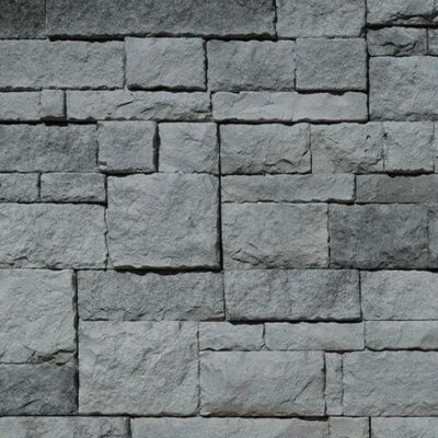 Aplacado de hormigón con textura de piedra irregular en tonos grises. Piezas rectangulares de diferentes formatos dispuestas en patrón de mampostería, acabado áspero y mate que imita la piedra natural.