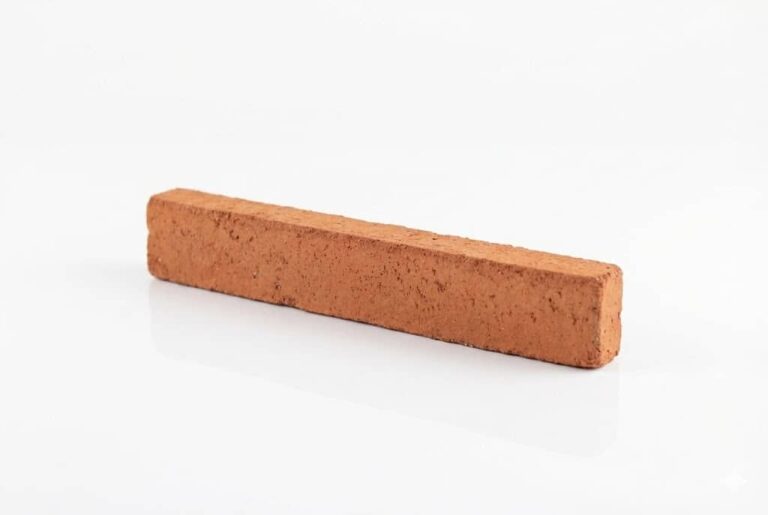 Pieza rectangular de ladrillo cerámico rústico en tonos rojos y naranjas, con textura rugosa y acabado mate. Material tradicional para revestimiento de pared.