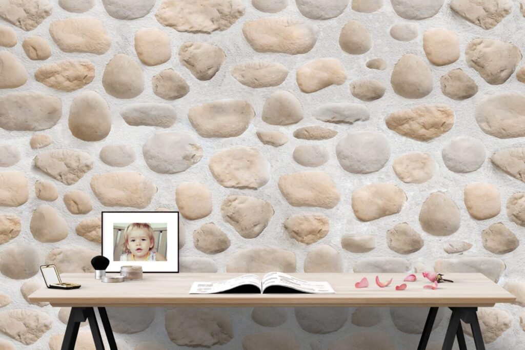 Espacio de trabajo minimalista con pared de revestimiento Mijares Plata con textura imitación piedra en tonos beige y gris claro. Escritorio de madera clara con patas negras, decorado con marco fotográfico, lámpara, libro abierto y pétalos de flor rosa.