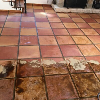 Espacio interior con suelo de gres de tonos terracota y marrones oscuros que muestran un acabado rústico envejecido. Las baldosas rectangulares presentan variaciones de color y pátina natural, típicas del suelo porcelánico imitación madera tradicional, con rejuntado en tono gris. La superficie refleja las condiciones de luz natural del ambiente.