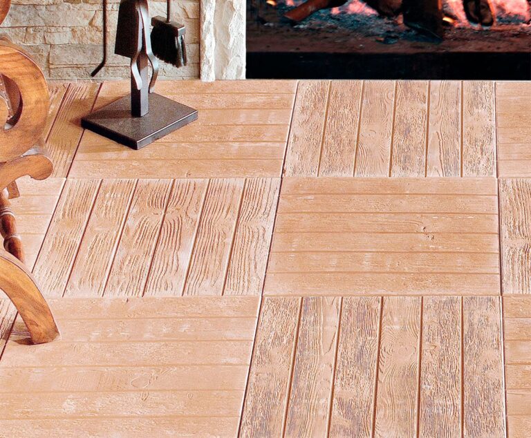 Salón con suelo de gres porcelánico imitación madera en tonos cálidos y claros, formato tabla rectangular, acabado mate con veteado natural. Al fondo, pared de piedra clara y escultura metálica sobre base gris.