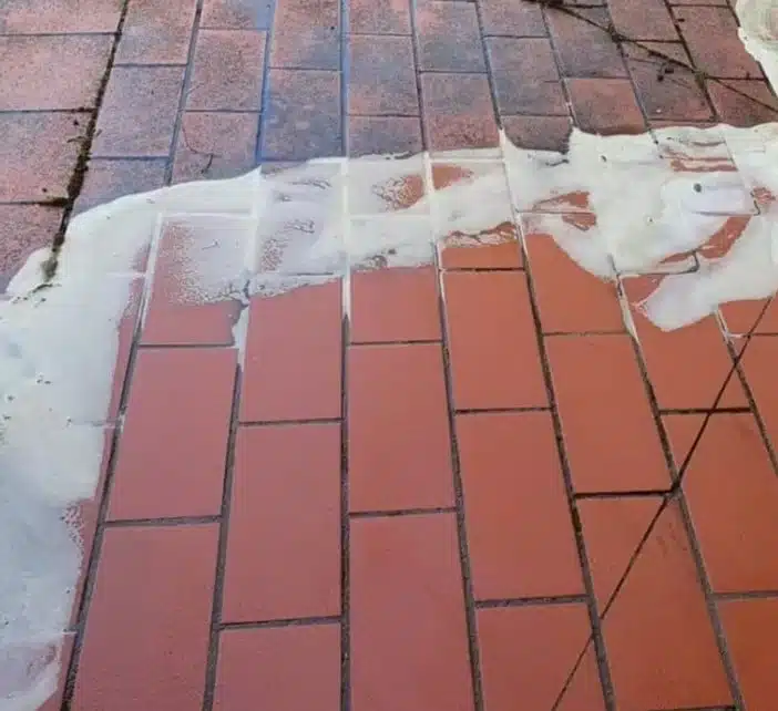 Persona limpiando un suelo de baldosas de exterior con un limpiador, demostrando el proceso de mantenimiento.