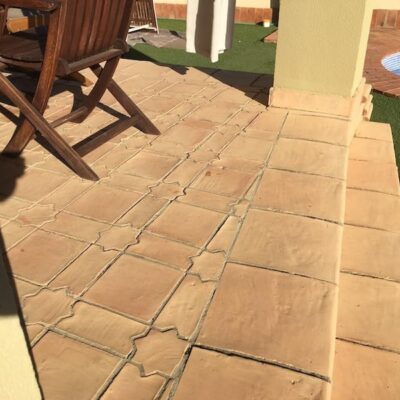 Terraza exterior pavimentada con suelo porcelánico imitación madera en tonos tierra, junto a piscina y zona ajardinada con césped artificial.