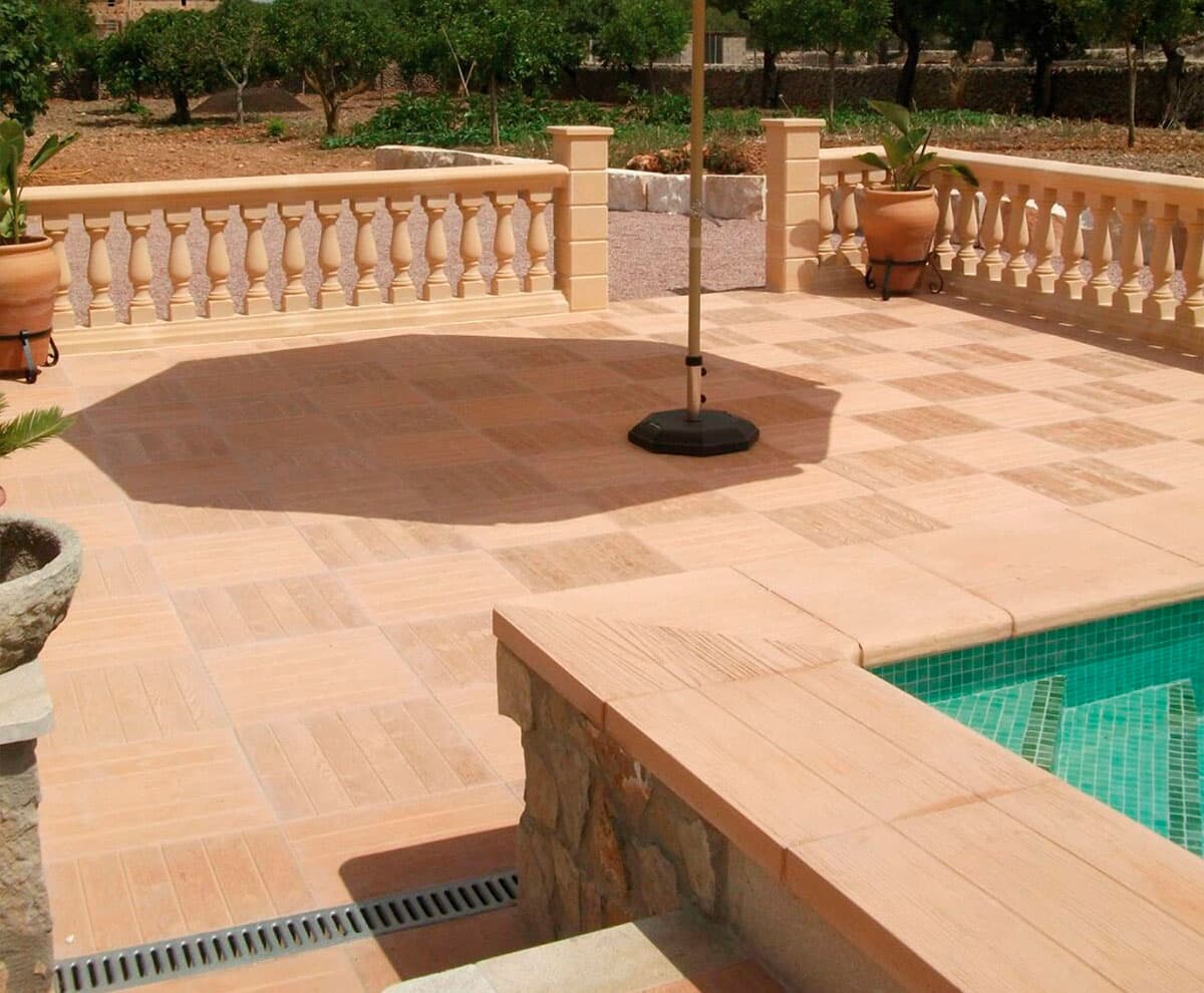 Zona de descanso intermedia entre terraza y piscina con tumbonas sobre baldosas de hormigón imitación madera.