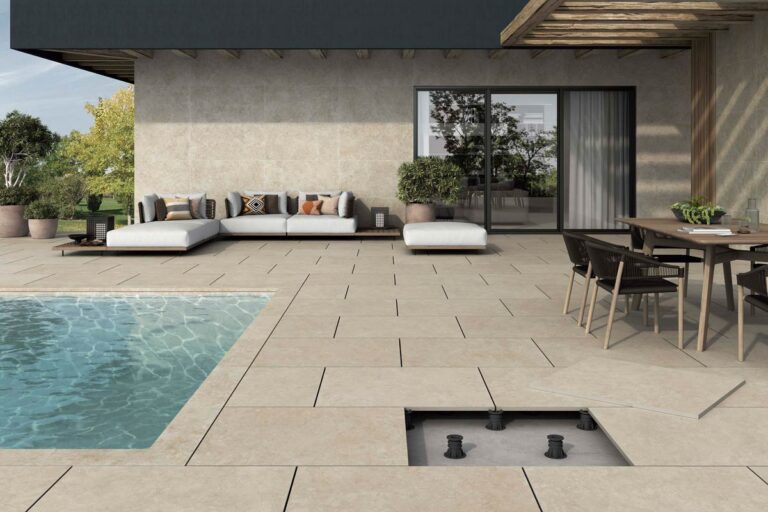 Terraza exterior con suelo porcelánico en tonos naturales beige y gris, junto a una piscina. La zona dispone de mobiliario de jardín moderno, pérgola de madera y acceso a la vivienda mediante puertas correderas de aluminio y cristal.