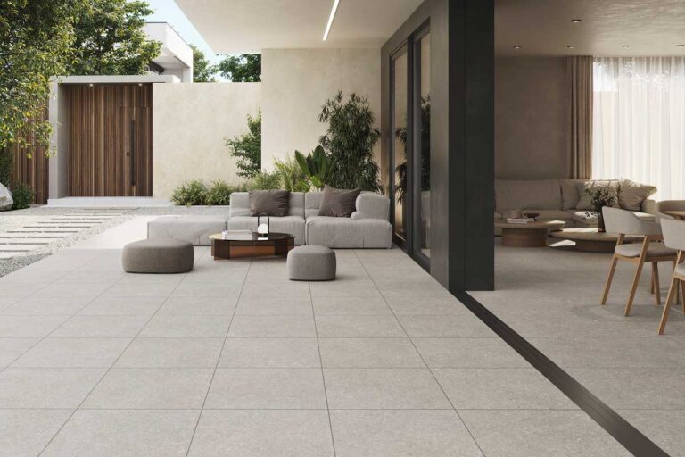 Terraza moderna con suelo porcelánico exterior efecto piedra natural en tonos grises, mobiliario de diseño contemporáneo y acceso directo a vivienda mediante puertas correderas de aluminio oscuro.