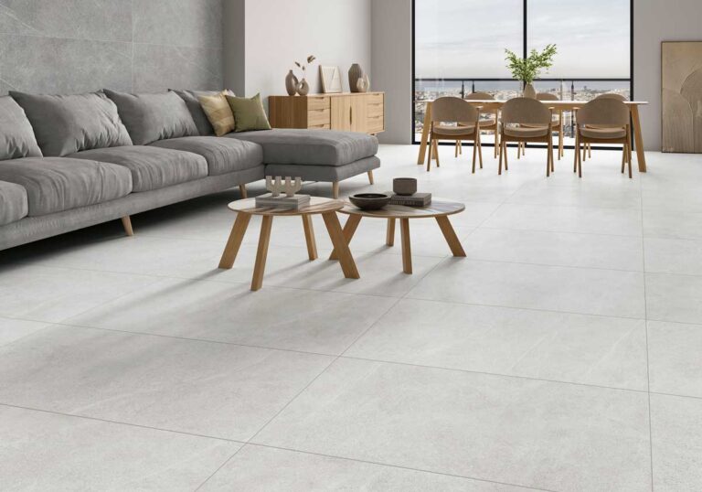 Salón contemporáneo con suelo de gres porcelánico en tonos grises claros imitando mármol, sofá gris con cojines, mesas auxiliares de madera y vistas panorámicas desde grandes ventanales.