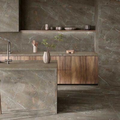 Cocina con suelo y revestimiento de pared en gres porcelánico imitación piedra natural en tonos grises, mobiliario de madera clara y encimera integrada con decoración minimalista.