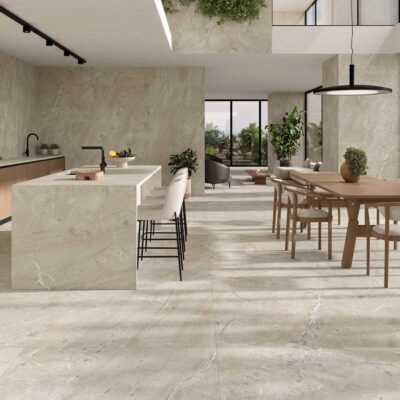 Cocina abierta y comedor contemporáneo con suelo cerámico de gran formato efecto piedra natural en tonos beige y grises. La zona cuenta con isla central, revestimiento de pared en mármol, ventanales amplios y mobiliario de madera clara.