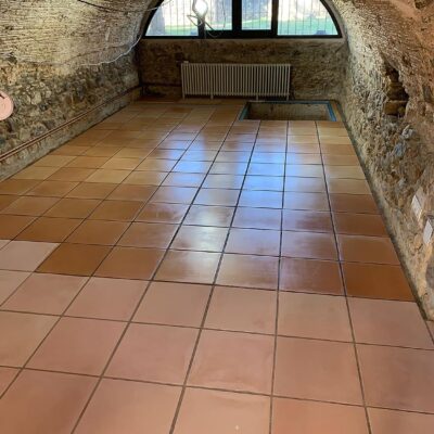 Espacio interior con bóveda de ladrillo y suelos porcelánicos en tonos terracota y beige con acabado mate, instalados en formato cuadrado. La estancia cuenta con radiador de hierro y ventana arqueada con vistas al exterior.