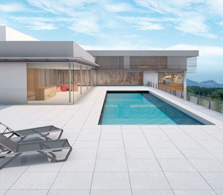 Terraza exterior de lujo con piscina rectangular, pavimento de gres porcelánico en tonos claros, zona de estar con loungers, casa contemporánea con grandes ventanales de cristal y vistas a montañas al fondo.