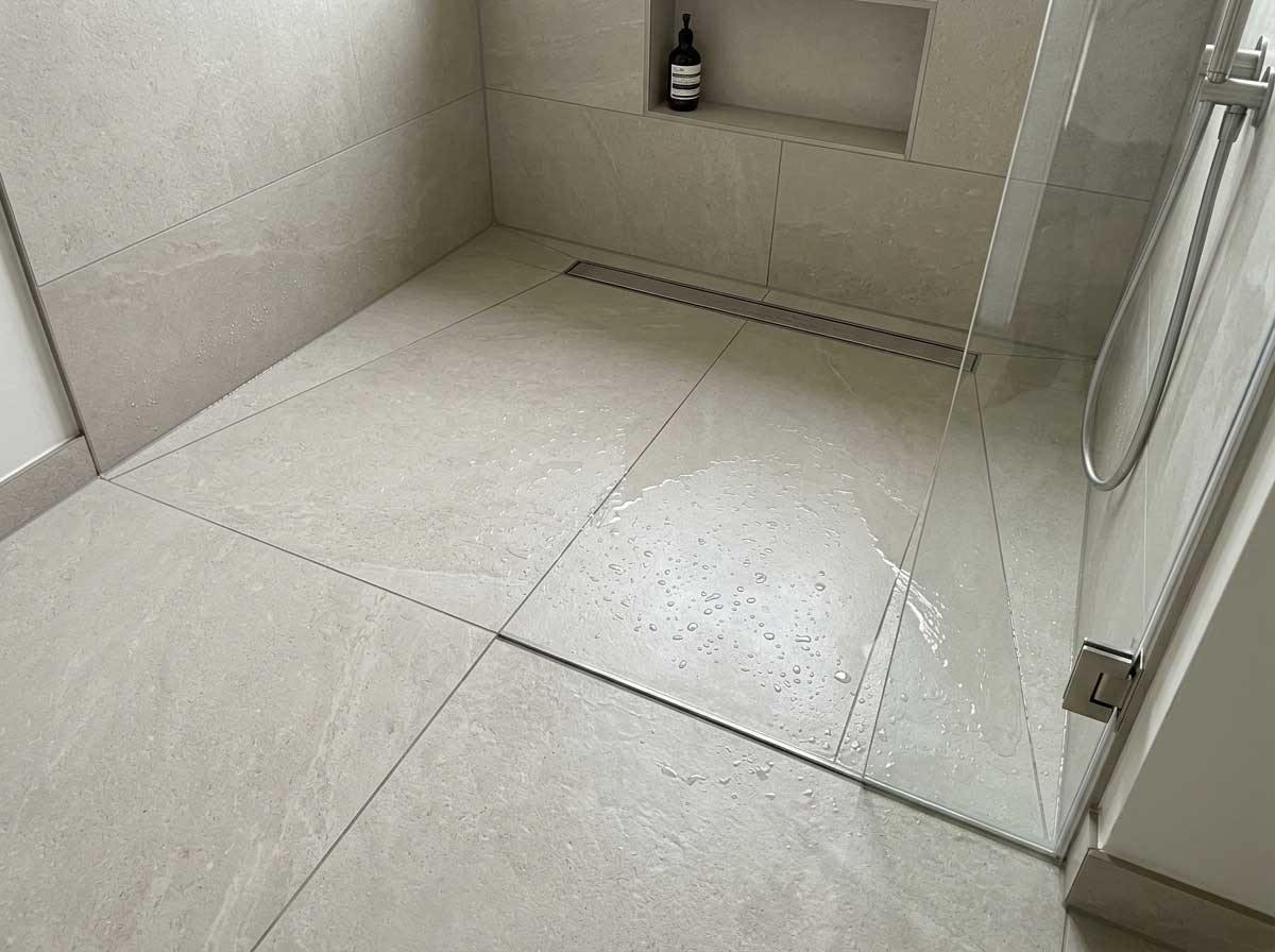 Plato de ducha de obra con pendiente hacia el desagüe y suelo porcelánico